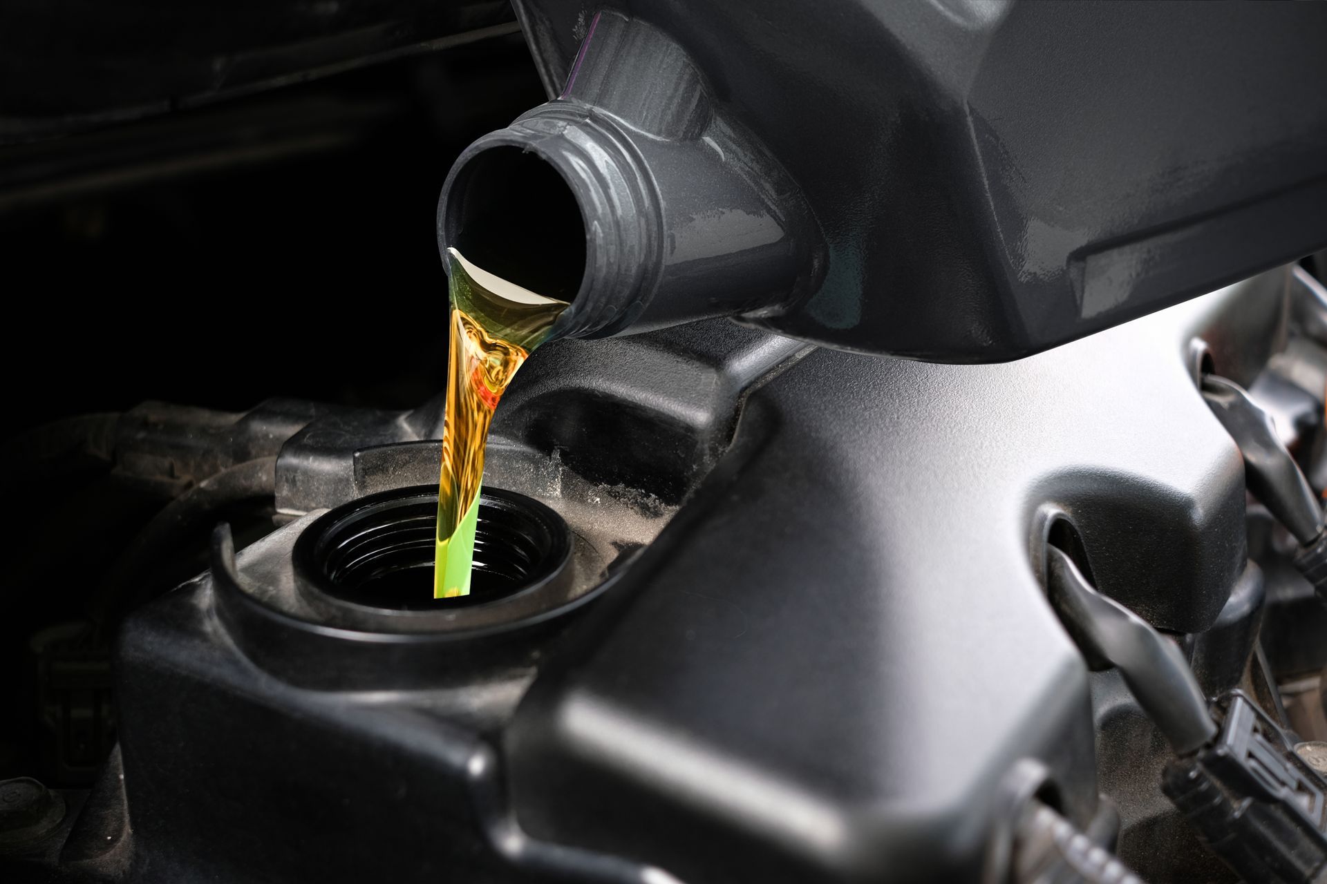 Motor oil being poured into a car engine fill port from a black bottle.