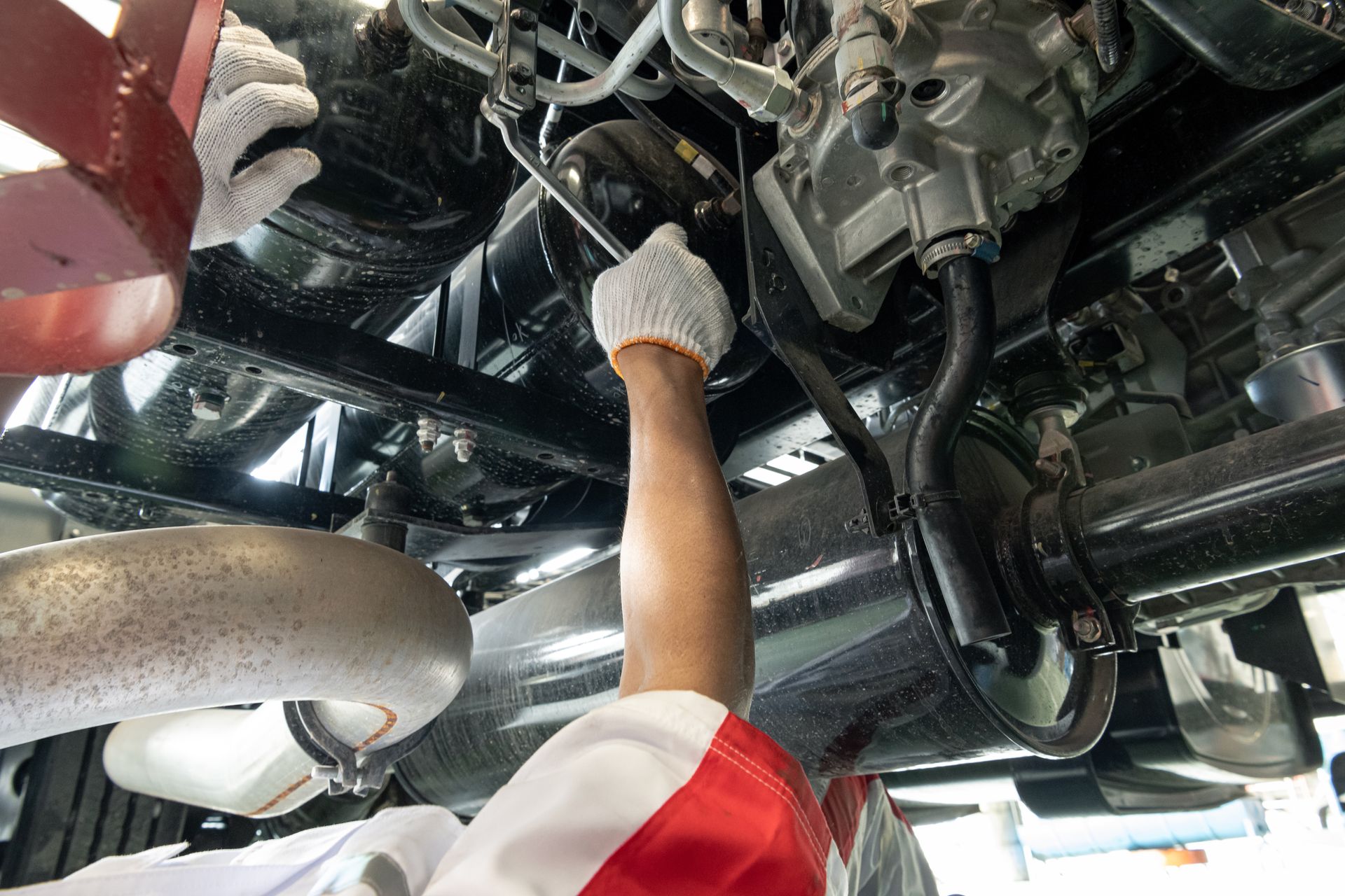 Mechanic reaching under a vehicle to inspect or repair engine components in a garage