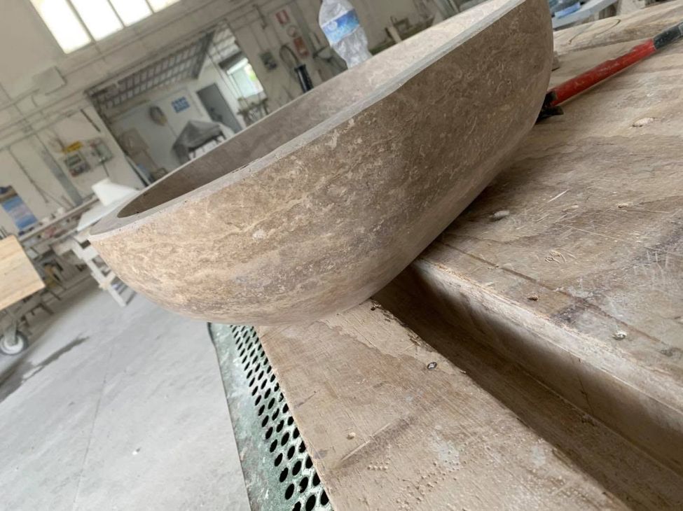 Bacino di pietra su un banco da lavoro impolverato in un'officina, con attrezzi e materiali sullo sfondo.