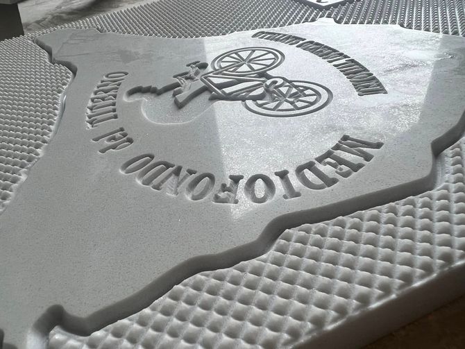 Primo piano di un emblema grigio in rilievo a forma di Texas con una motocicletta e testo arcuato su una superficie ruvida.