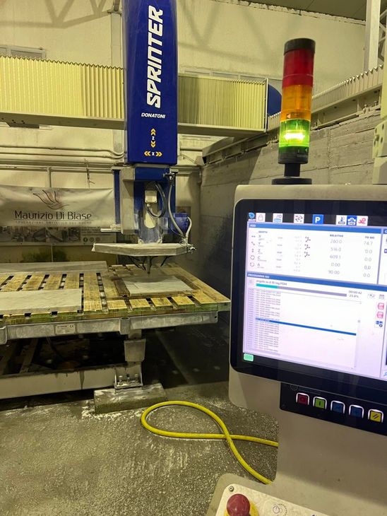 Macchina da taglio industriale con pannelli di legno impilati, schermo di controllo e spia luminosa di segnalazione rossa-gialla-verde.
