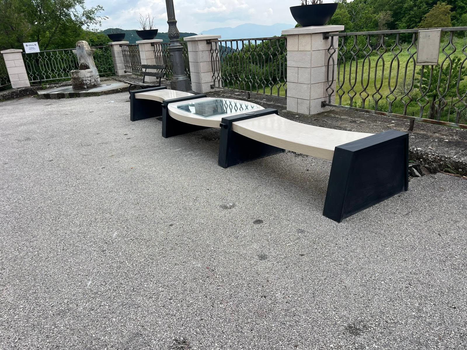 Panchina in pietra da esterno con tavolo in vetro su una terrazza di ghiaia con vista panoramica.
