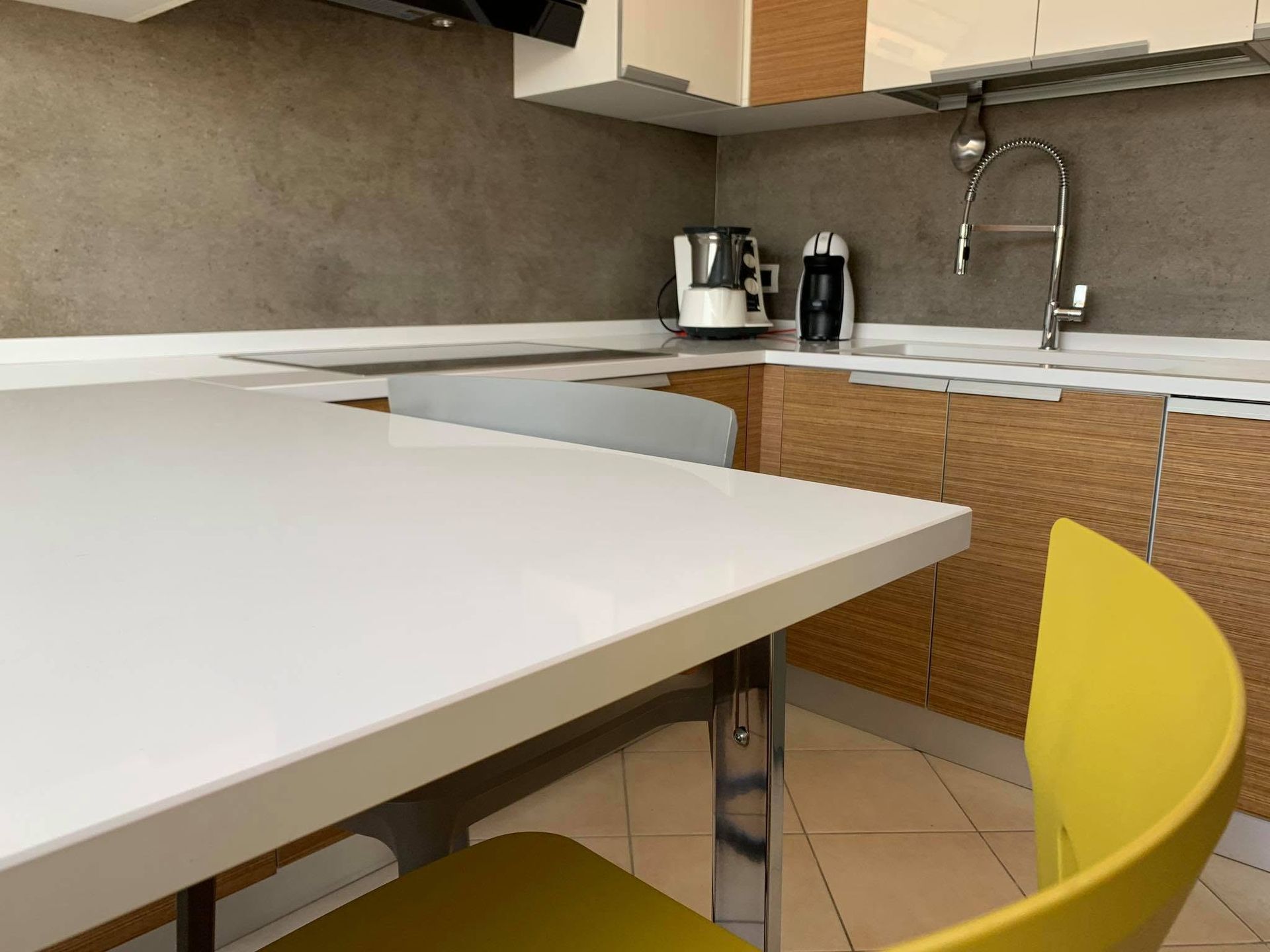 Cucina moderna con tavolo bianco, sedia gialla e zona lavello con bollitore e macchina per il caffè.