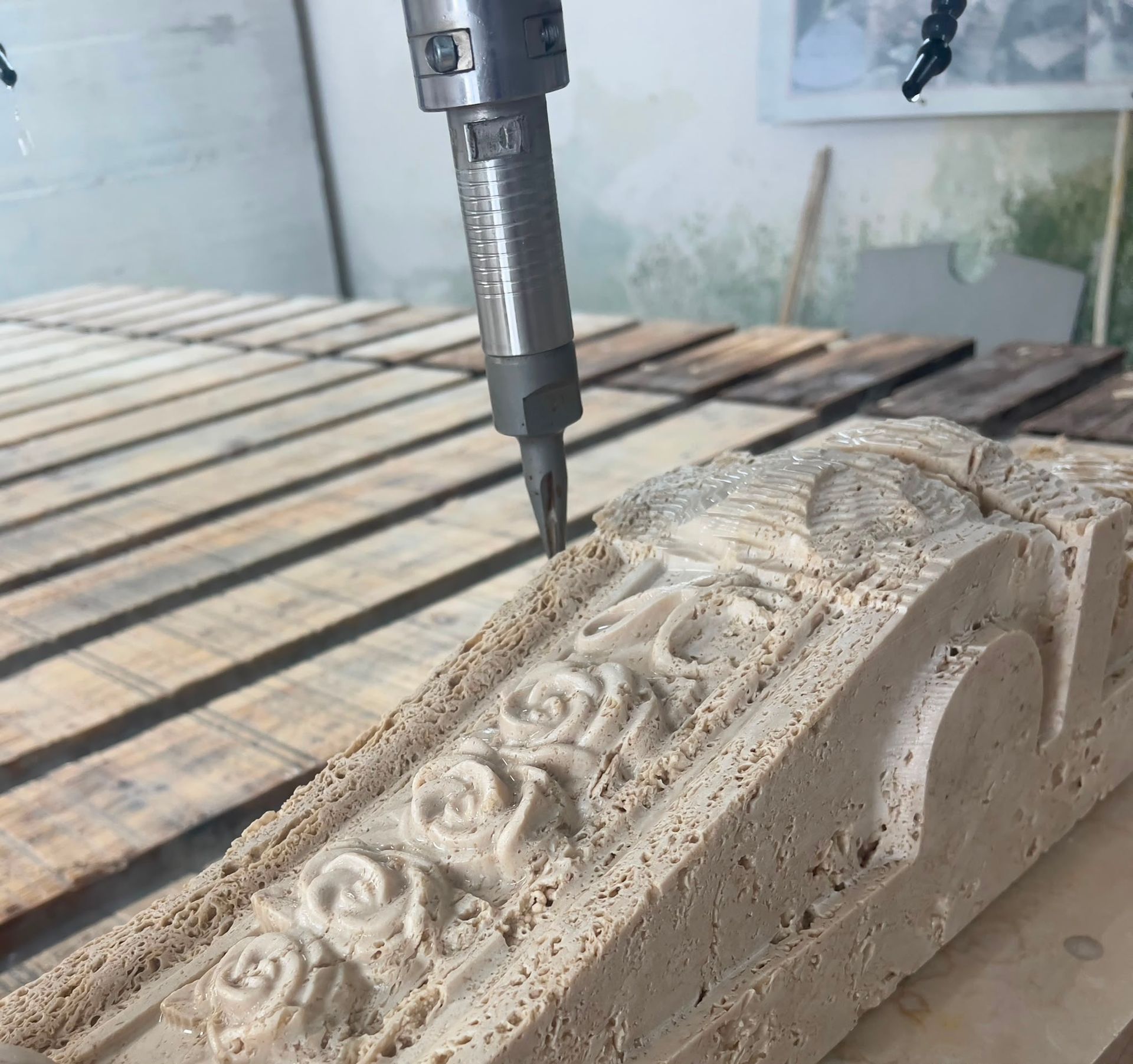 Una fresatrice CNC incide un elaborato motivo floreale su un pannello di legno beige su un tavolo da officina.