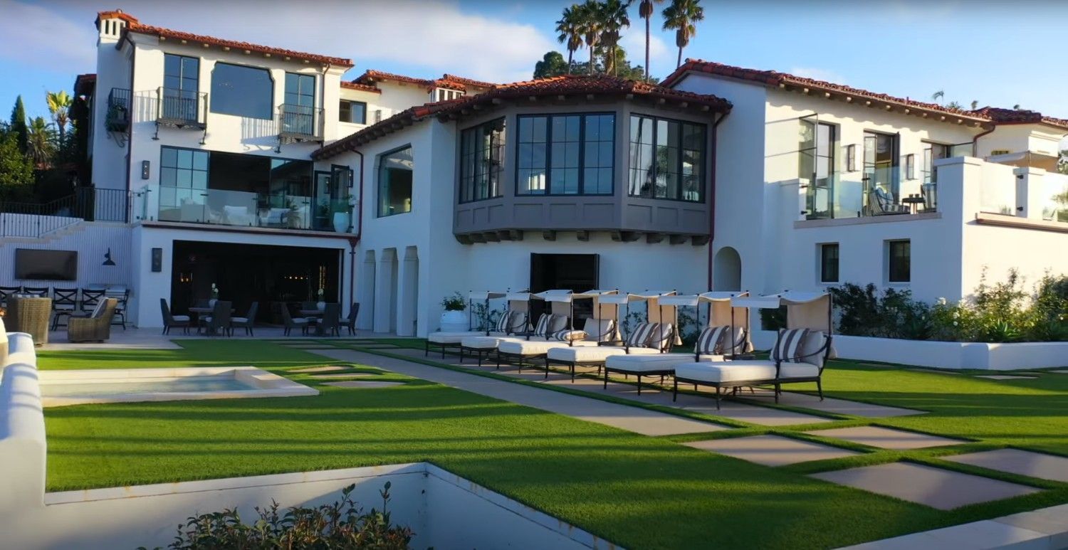 A large white house with a lot of windows is sitting on top of a lush green lawn.