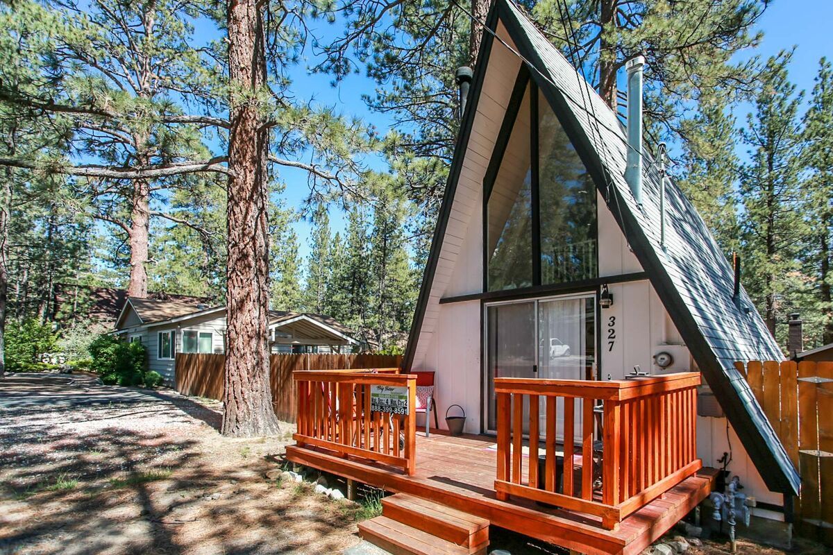 A small a frame cabin with a deck in the middle of a forest.
