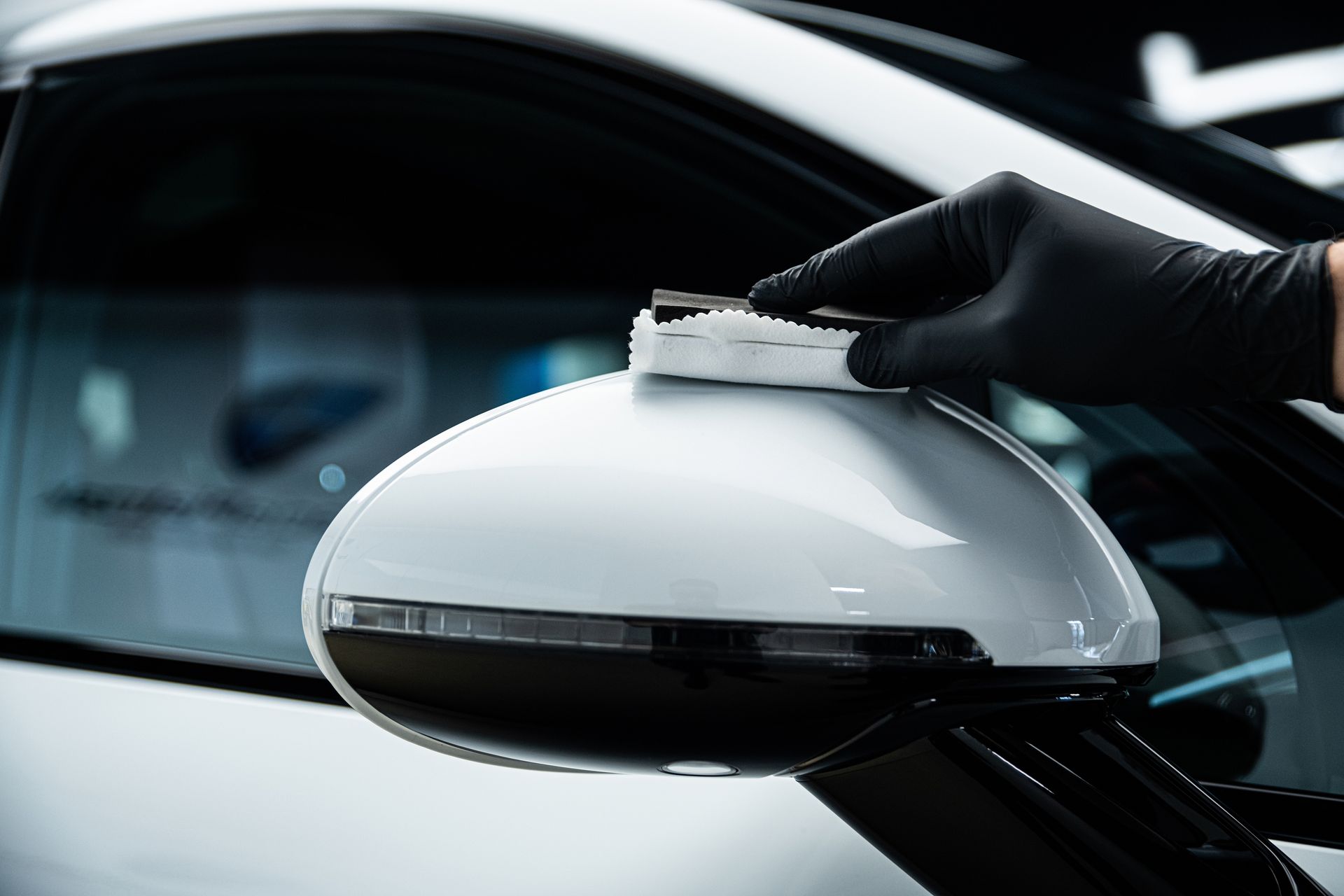 Gloved hand wiping a white car side mirror with a cloth