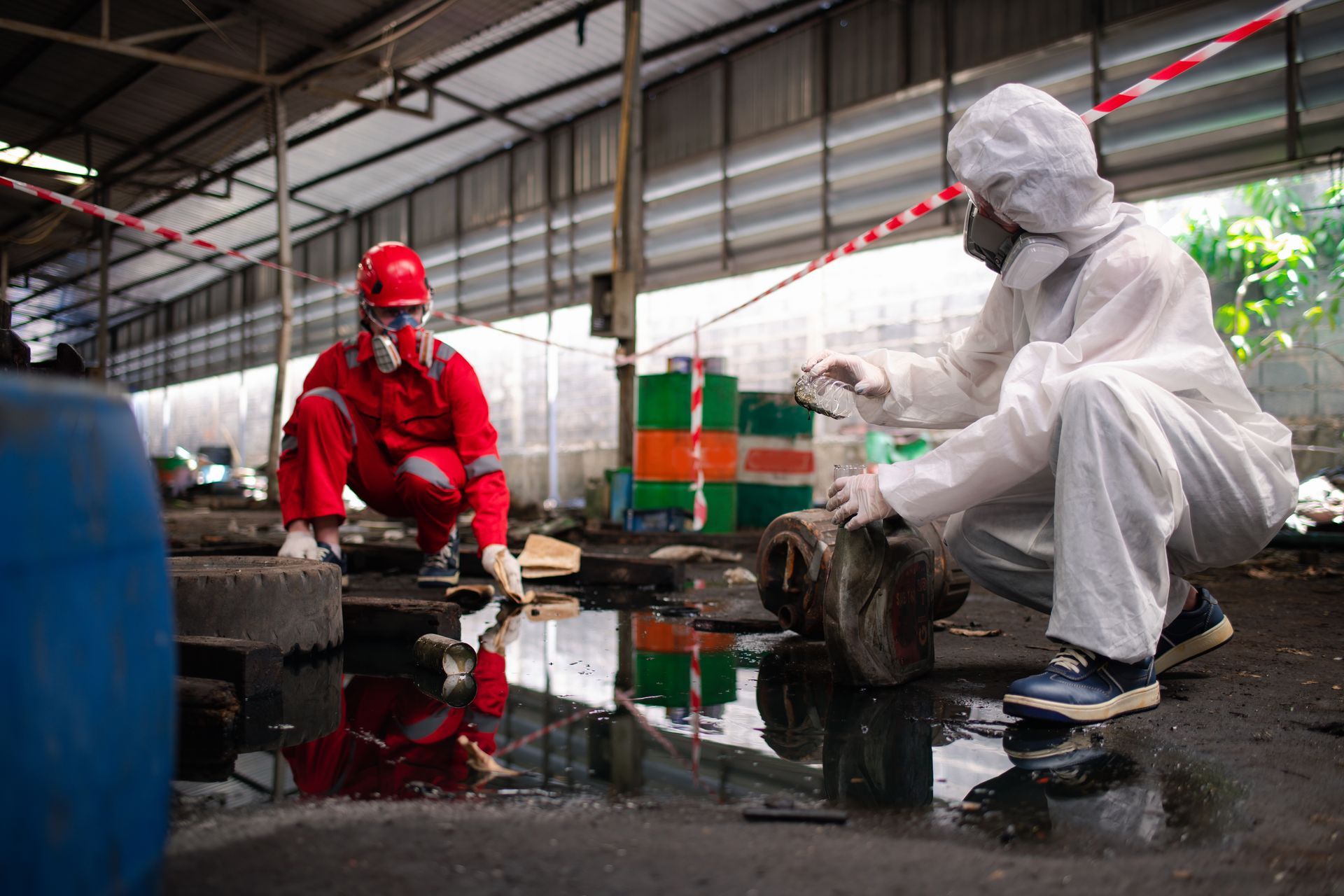 Two workers in protective suits cleaning an industrial spill indoors, one in red and one in white