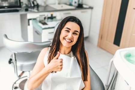 A gloved professional points to a specific area on a panoramic dental X-ray displayed on a screen.