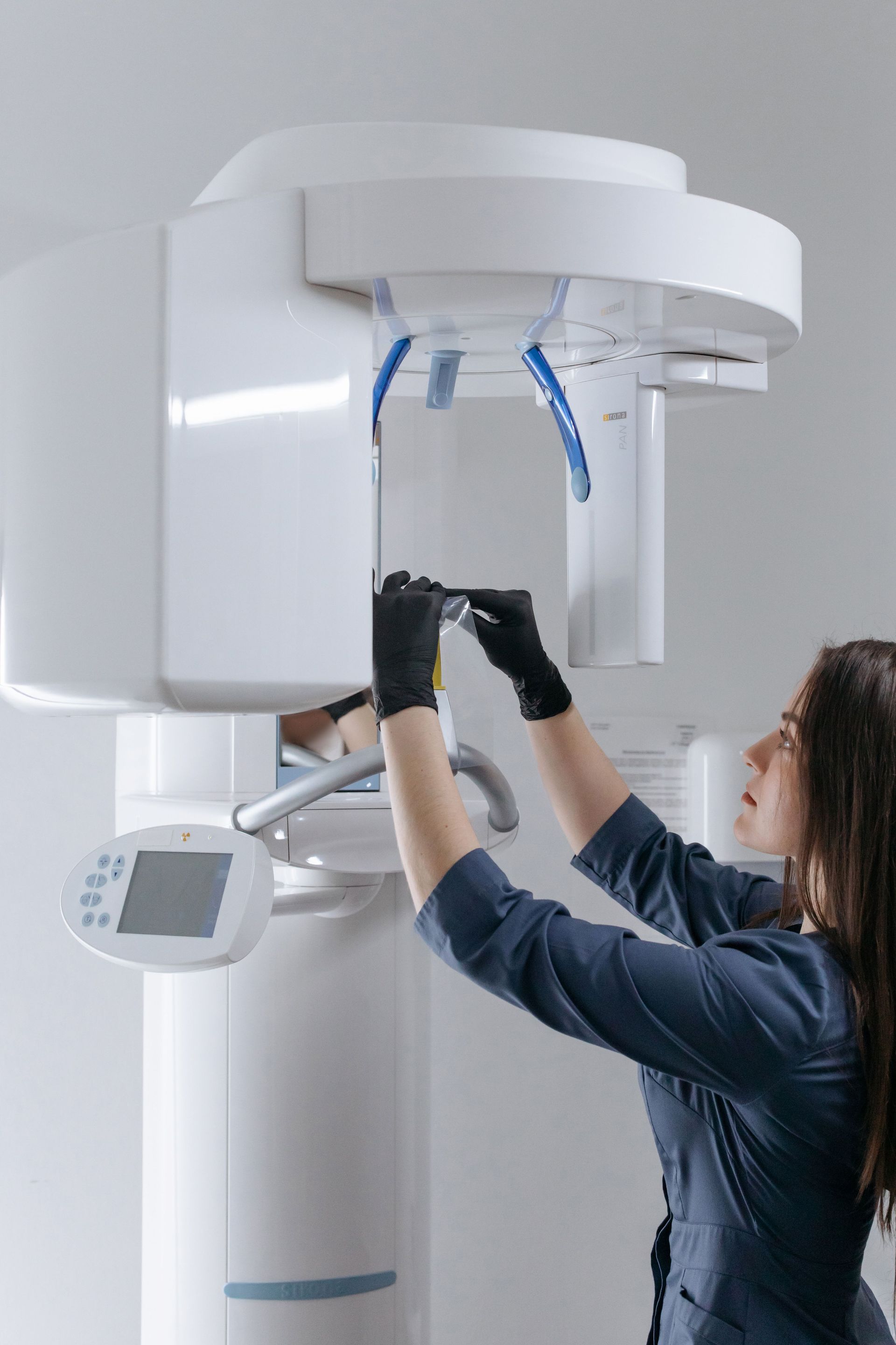 A gloved professional points to a specific area on a panoramic dental X-ray displayed on a screen.