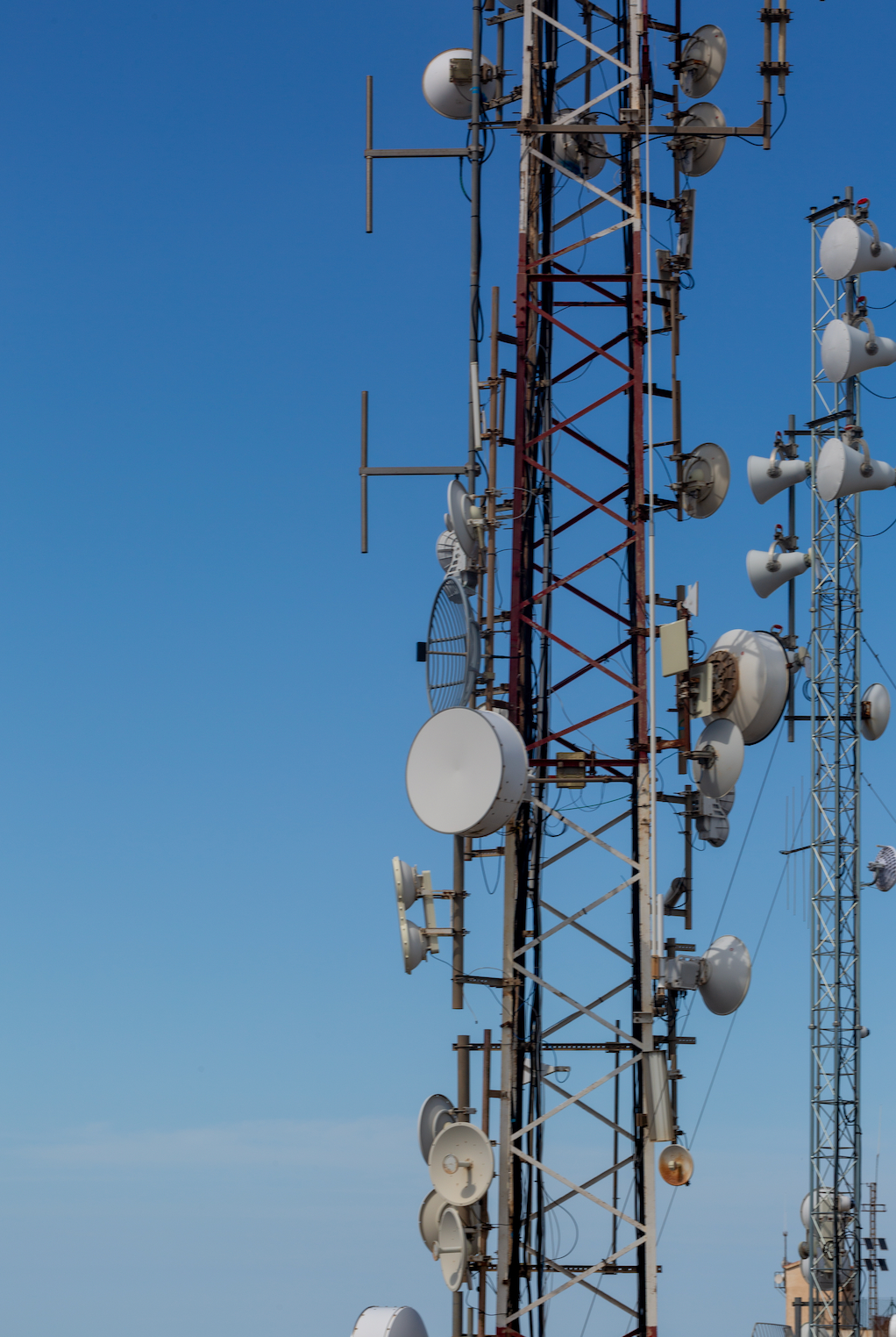 Telecommunication towers against a bright blue sky, covered with various antennas and equipment.