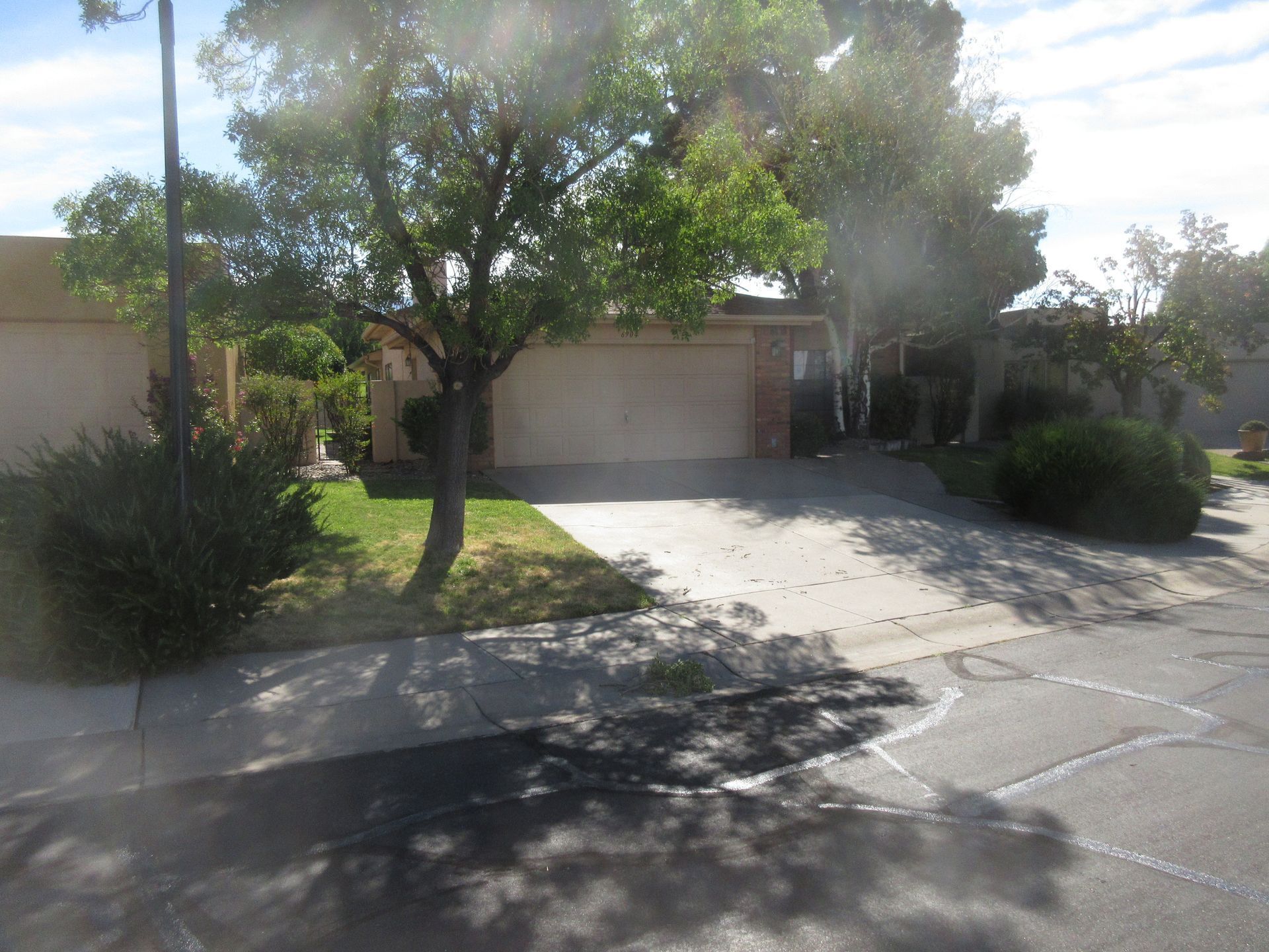 A residential home with a driveway and garage, trees and bushes in front, with a blue sky.