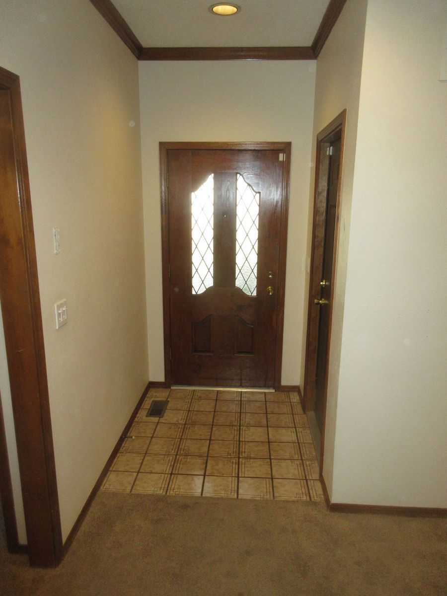 Entryway with brown wooden door, beige walls, and tile floor. Another door is to the right.