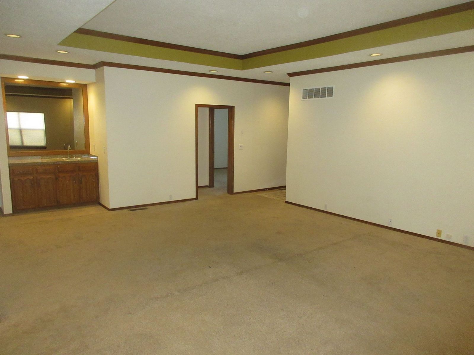 Empty room with beige carpet, walls, and trim. Features a bar area and a doorway.