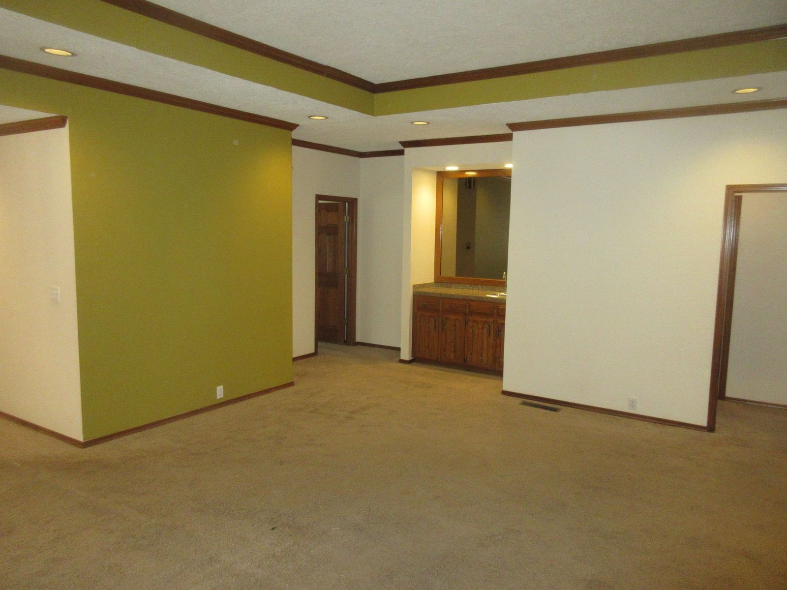 Empty room with green and beige walls, wood trim, built-in bar, and tan carpet.