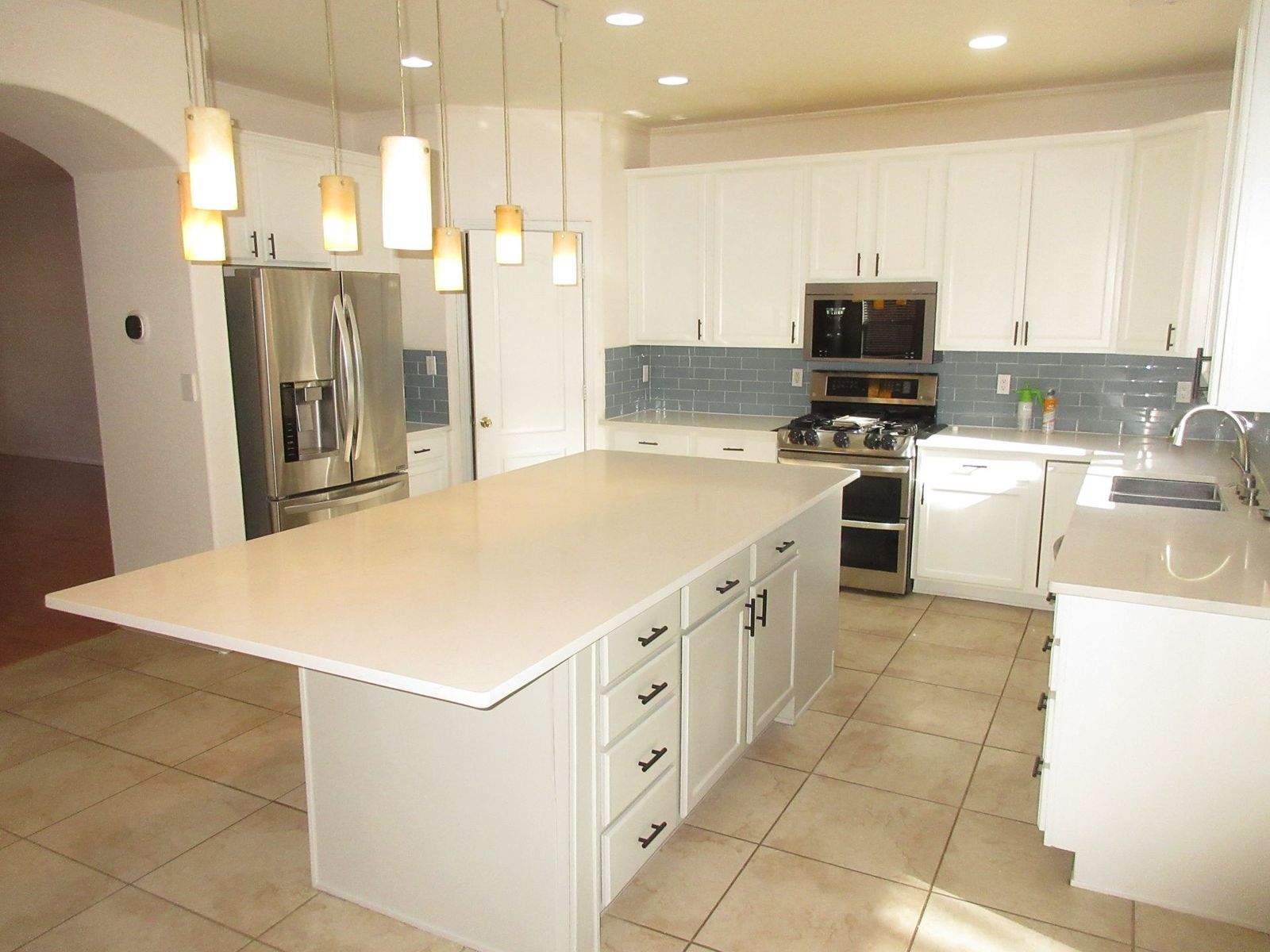Bright white kitchen with large island, stainless steel appliances, and tile floor.