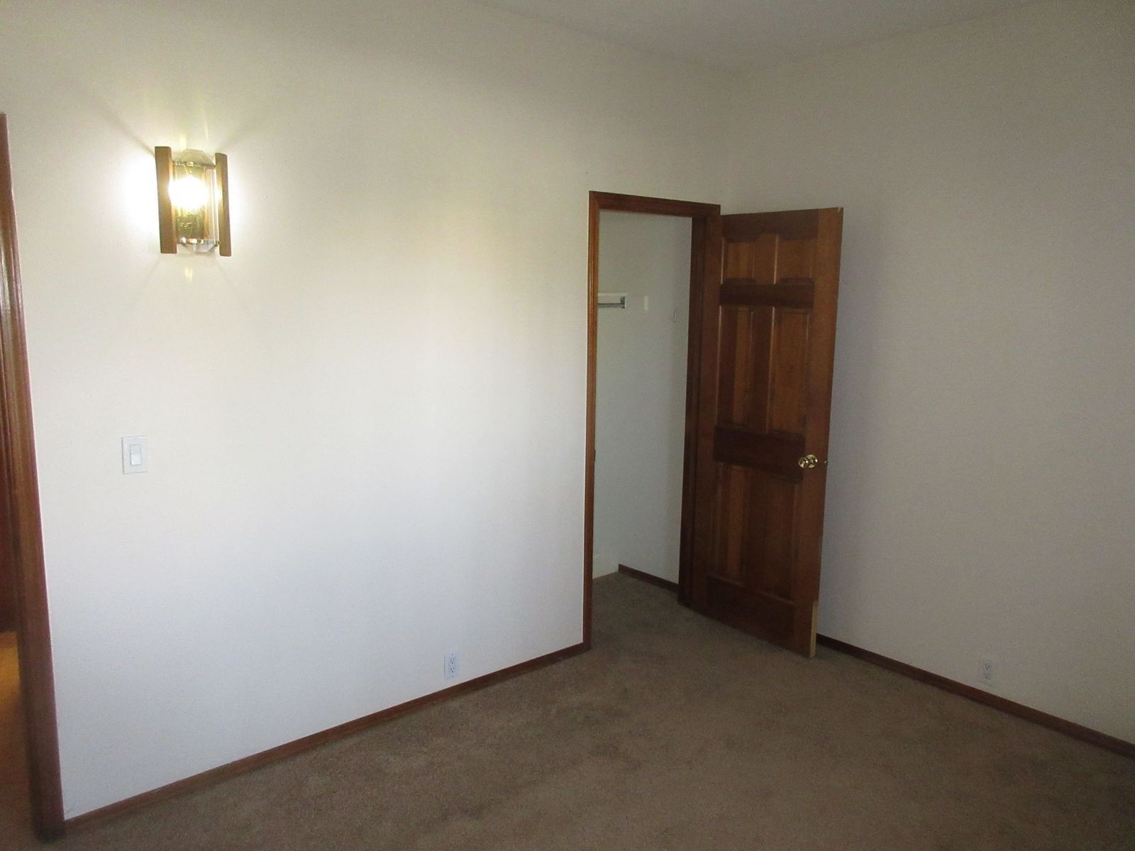 Empty room with a brown carpet, white walls, and a wooden door slightly ajar.