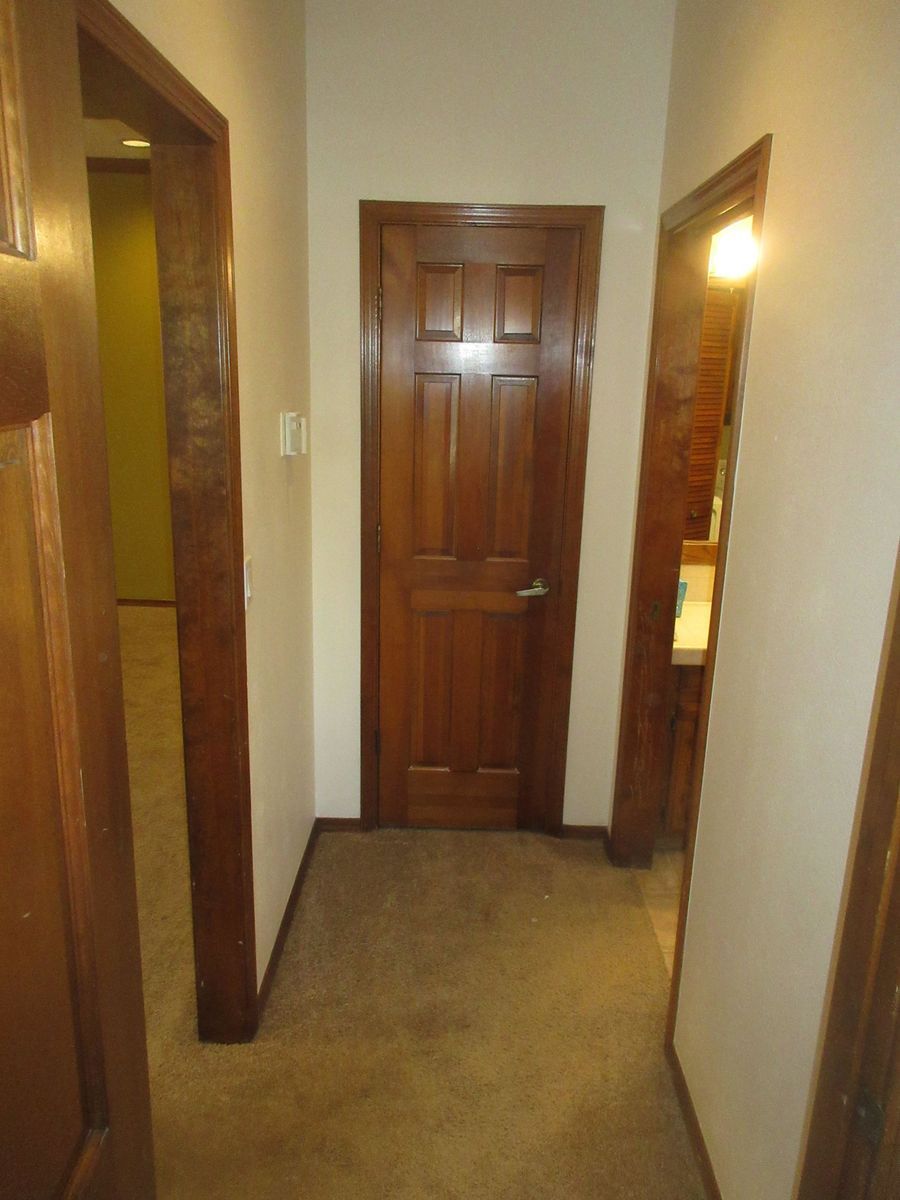Hallway with three wooden doors, carpet floor, beige walls.