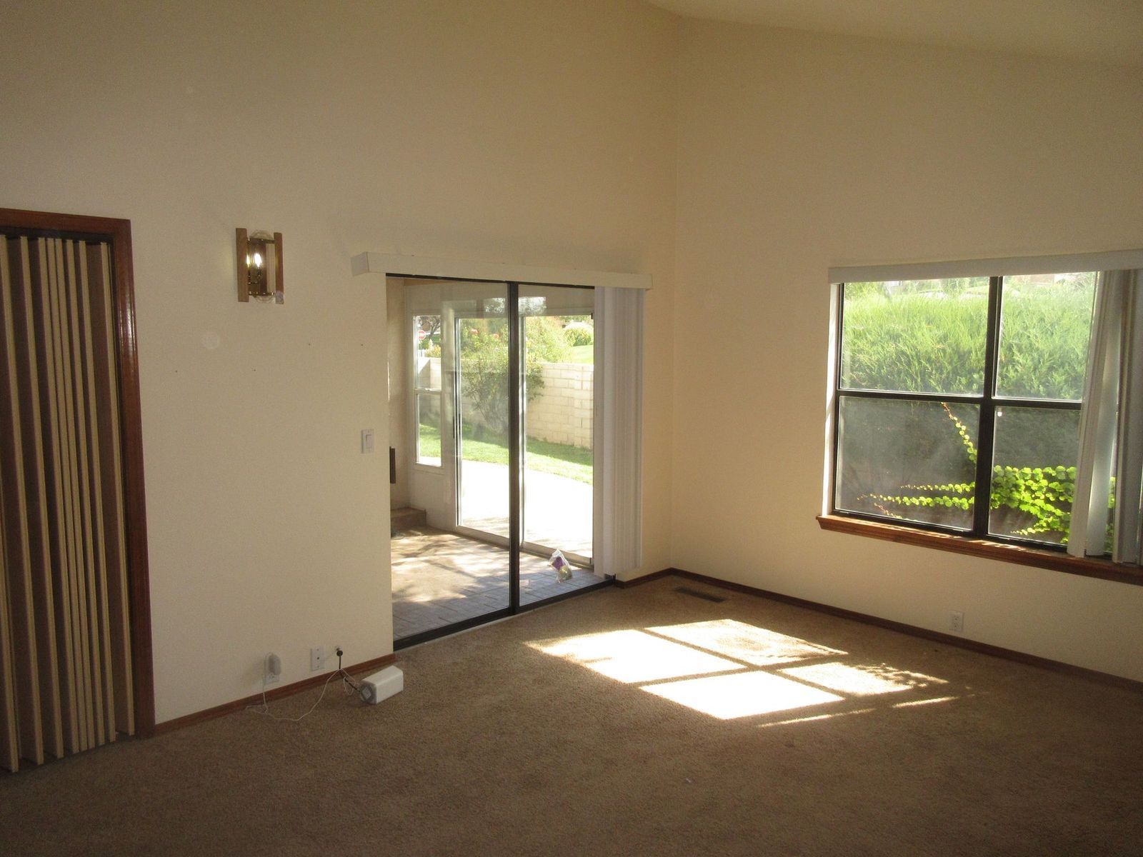 Empty living room with sliding glass door and window, beige walls, brown carpet.