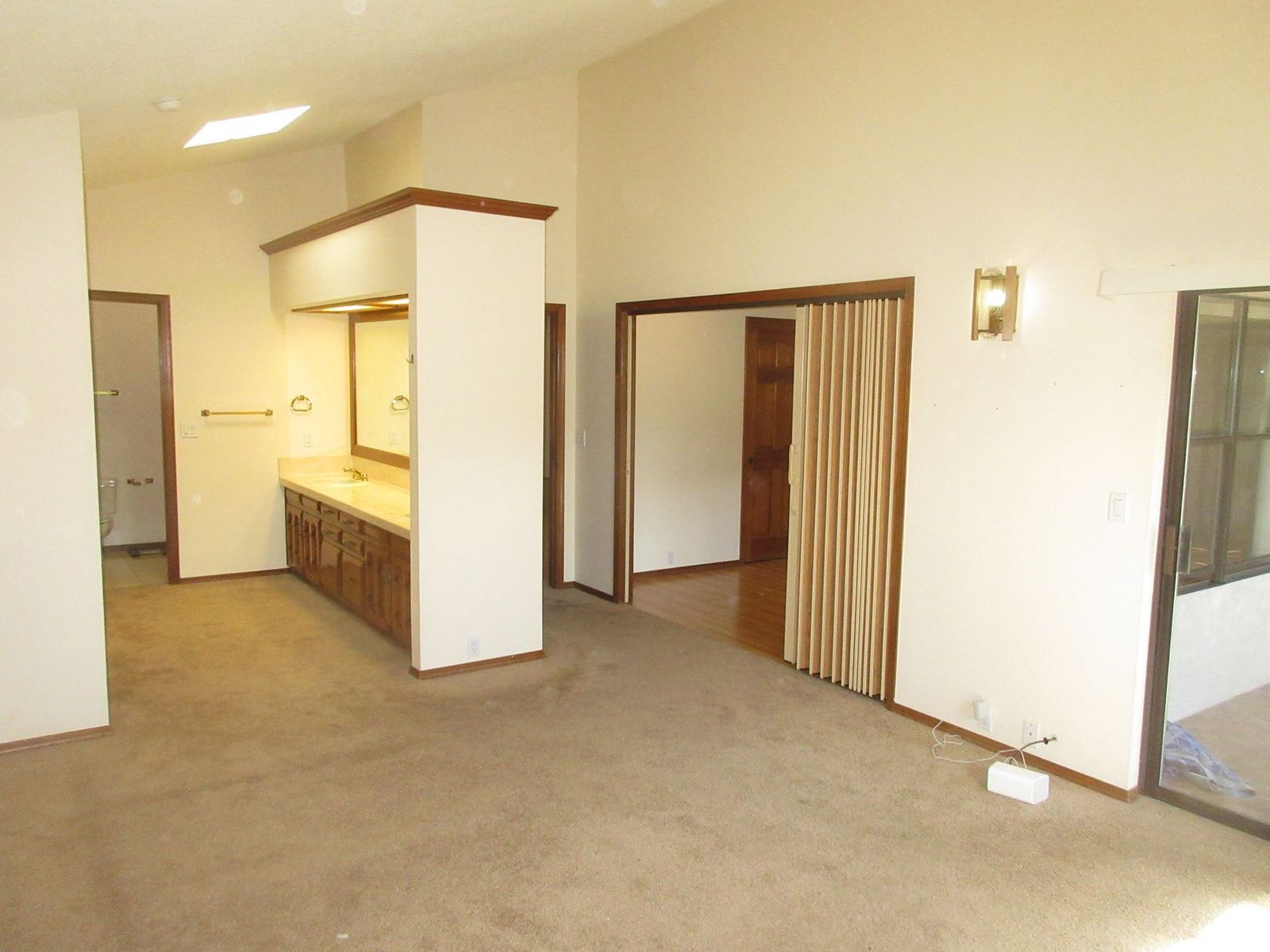 Empty room with brown carpet, multiple doorways, a bathroom vanity, and a window.