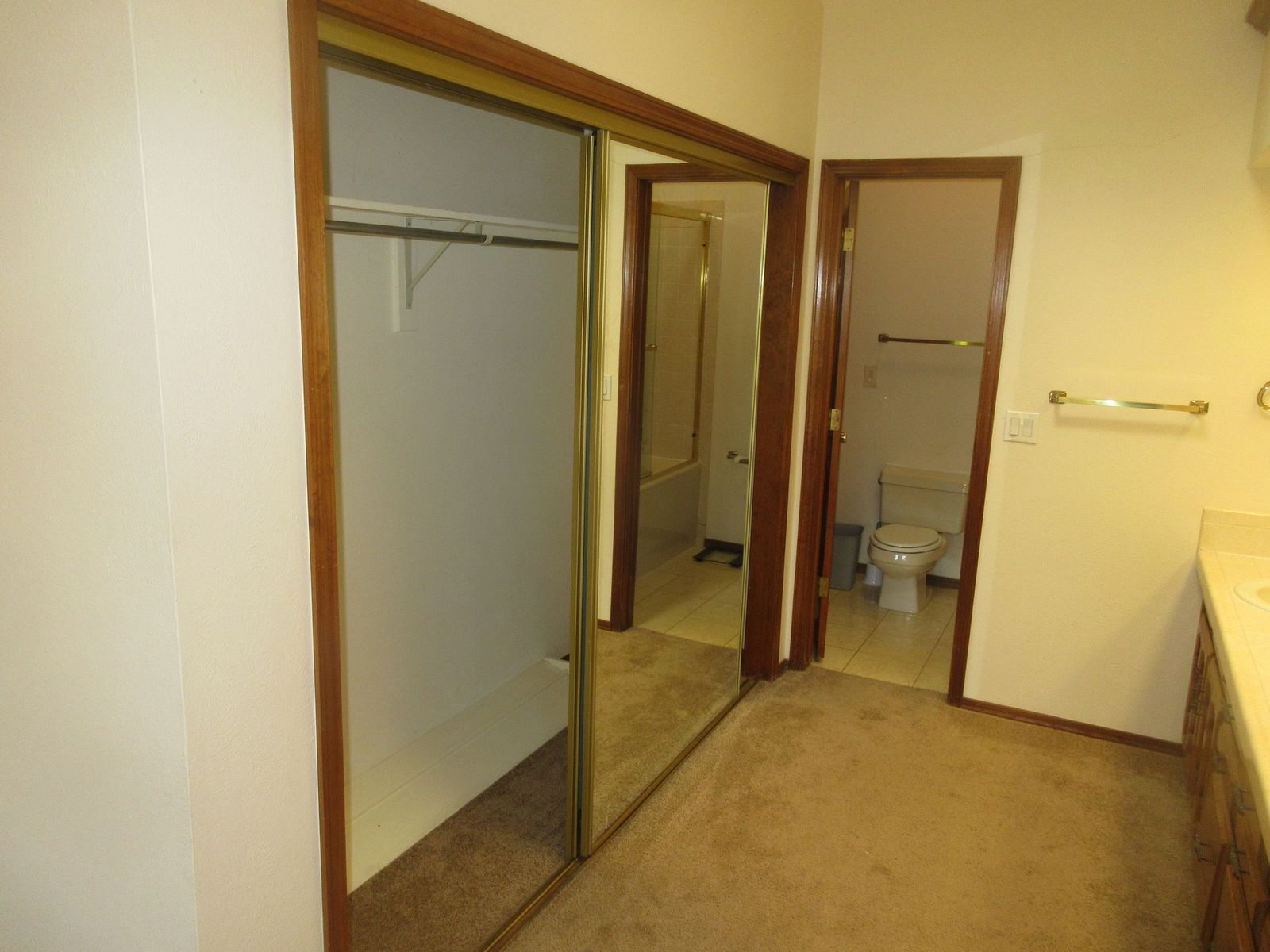 Bedroom with closet and bathroom door, tan carpet, cream walls, gold trim.