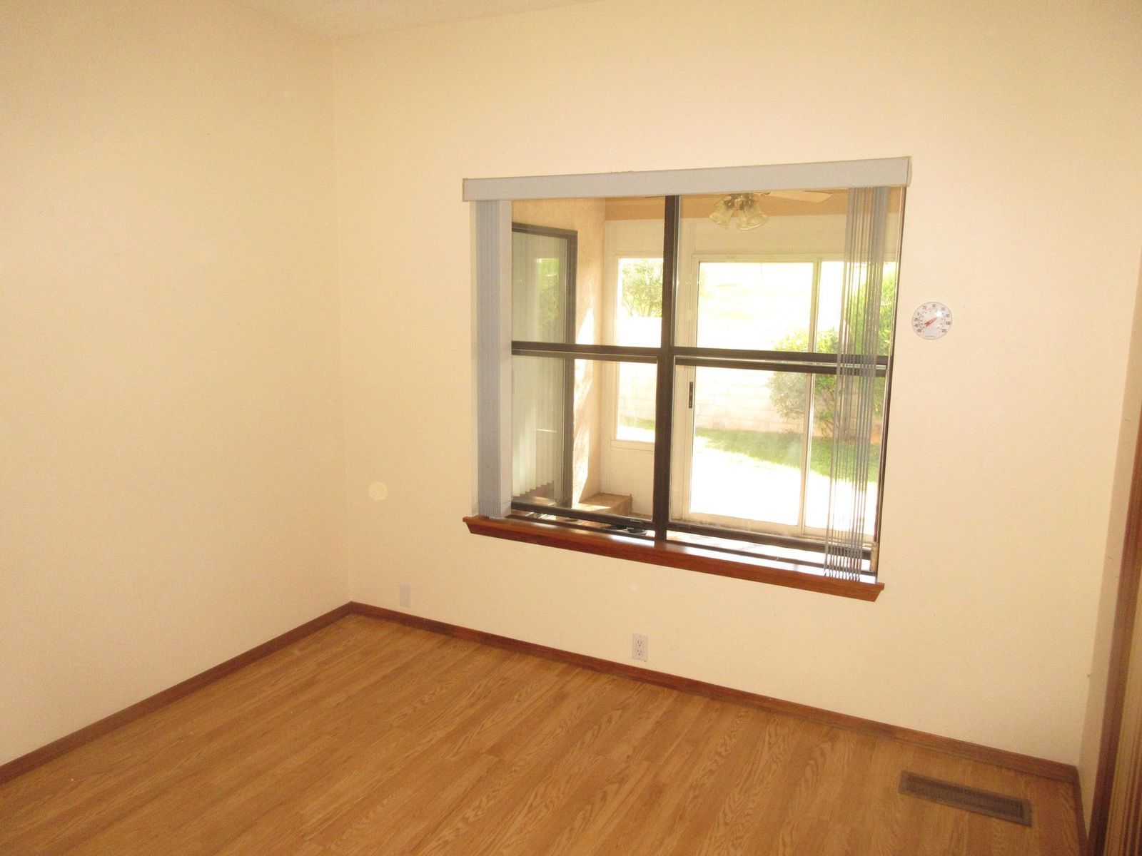 Empty room with wooden floors, tan walls, and a window overlooking a yard.