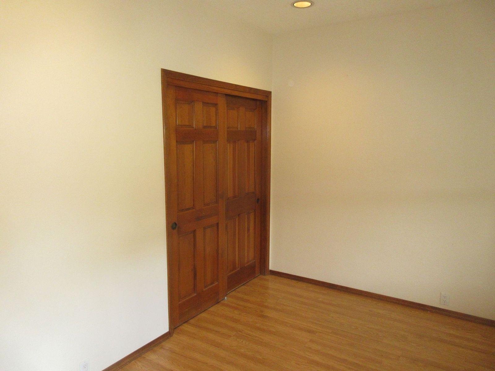 Wooden closet doors in a room with light-colored walls and hardwood floor.