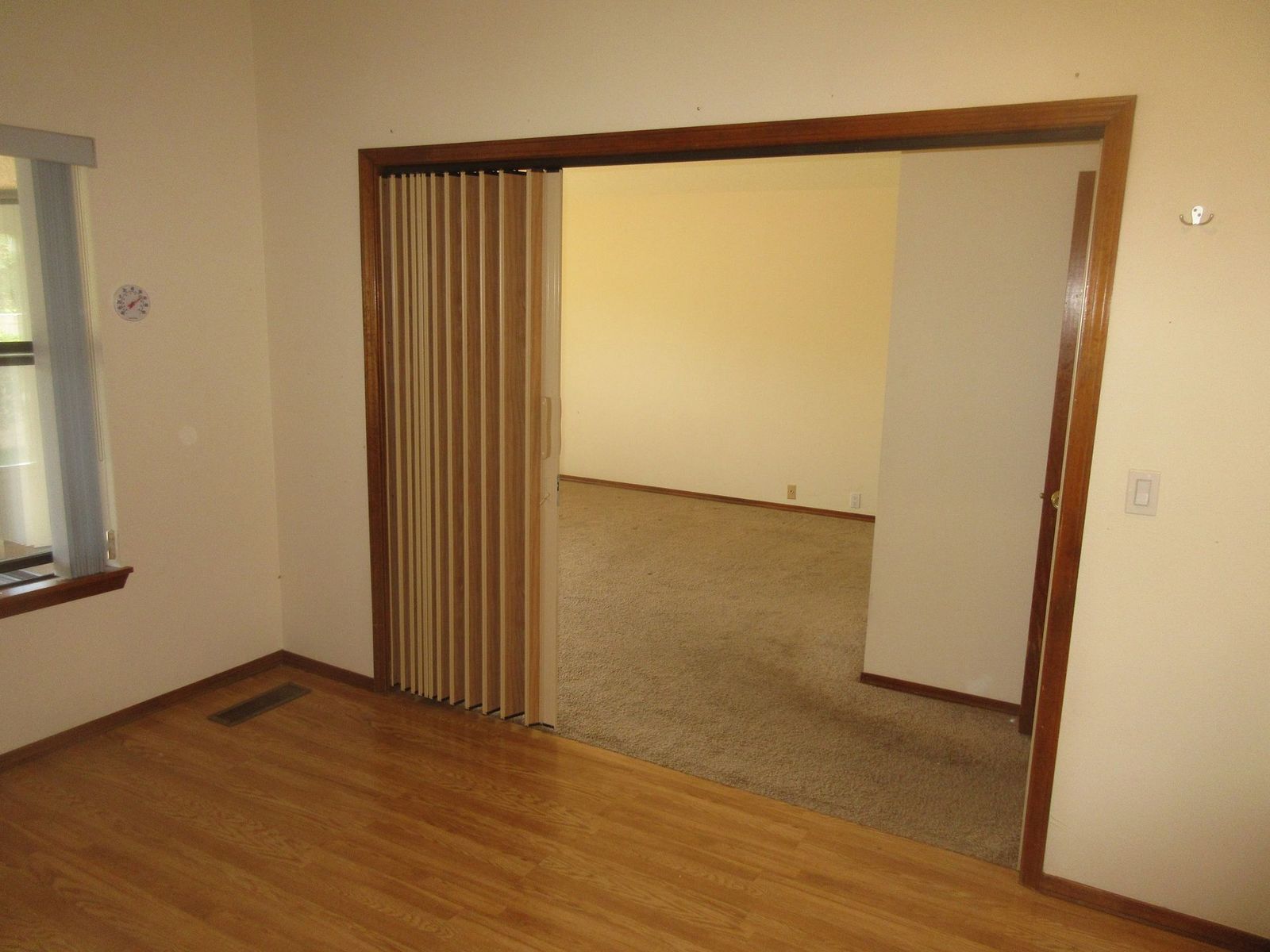 Interior view: room with a closed, accordion-style folding door, leading to a room with carpet and a window.