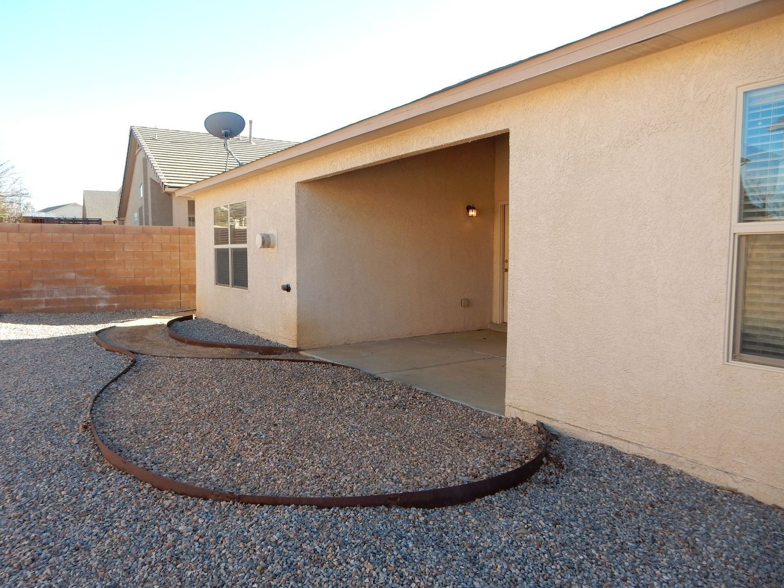 Backyard with gravel ground, covered patio, and house in the background. Brown edging surrounds a gravel garden bed.