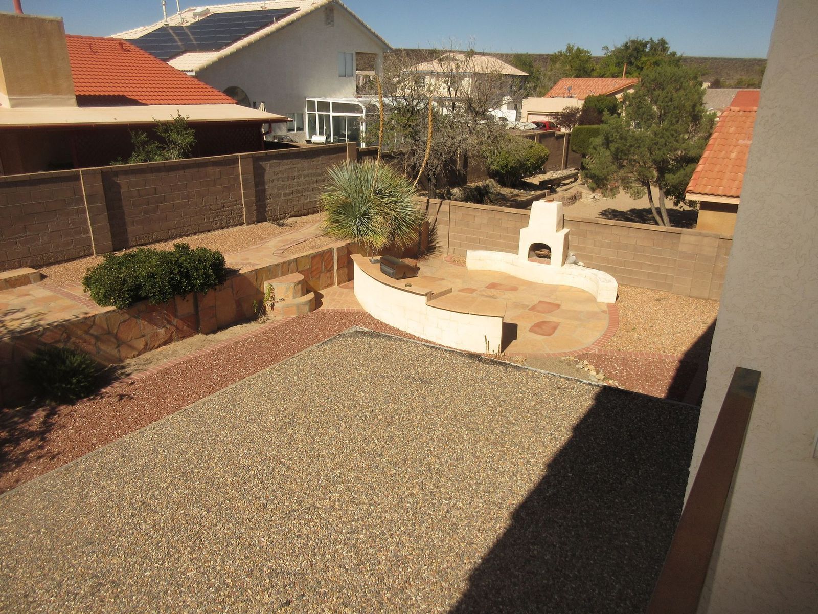 Backyard with gravel, stone patio, brick oven, and surrounding homes.