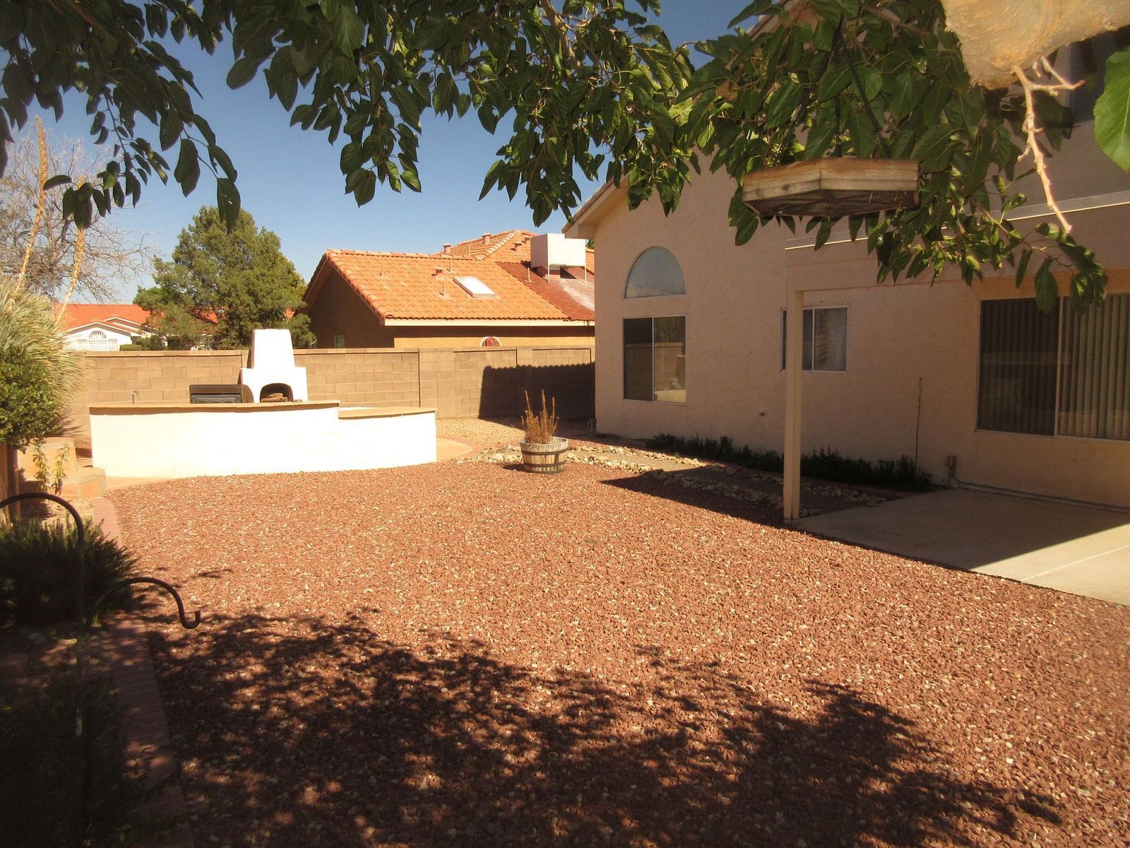 Backyard with gravel ground, fire pit, and building with brown roof.
