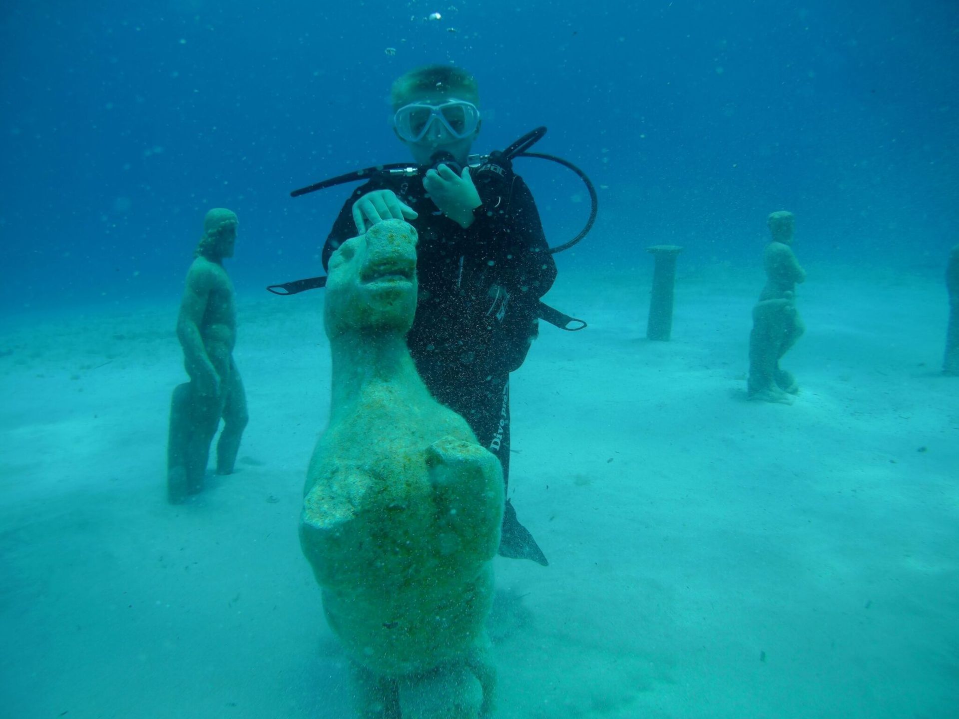A scuba diver is standing next to a statue in the ocean.