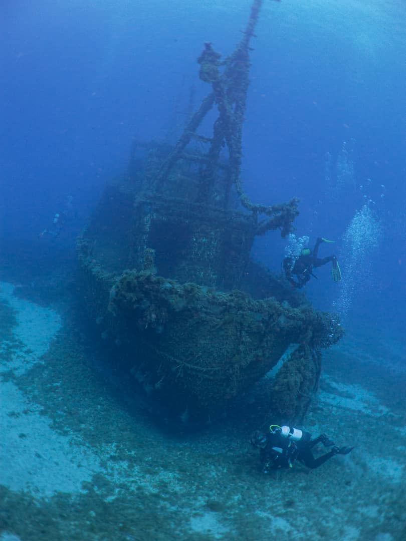 A group of scuba divers are swimming around a shipwreck in the ocean.