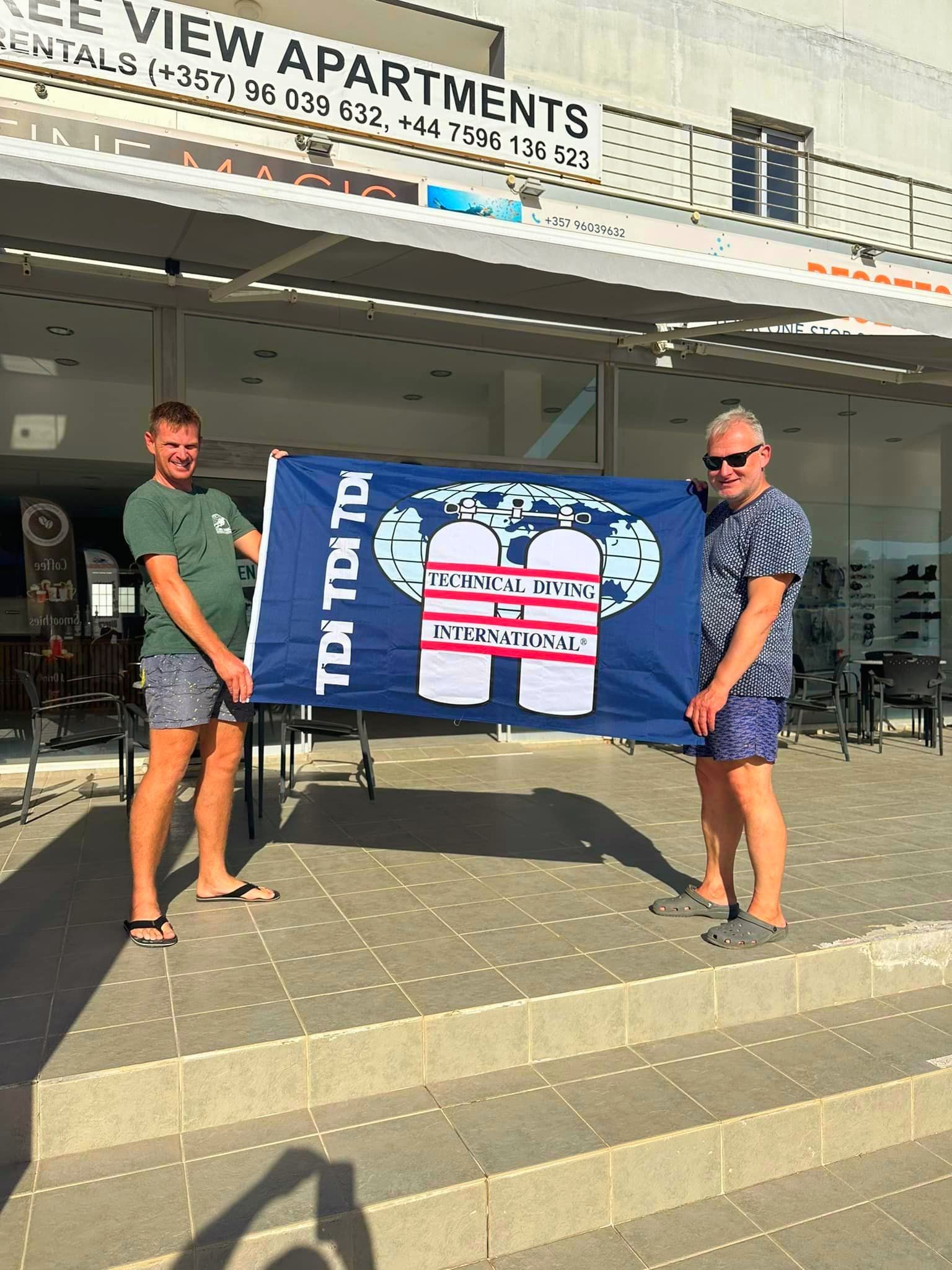 Two men are holding a flag in front of a building.