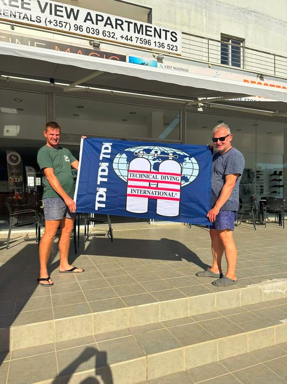 Two men are holding a flag in front of a building.
