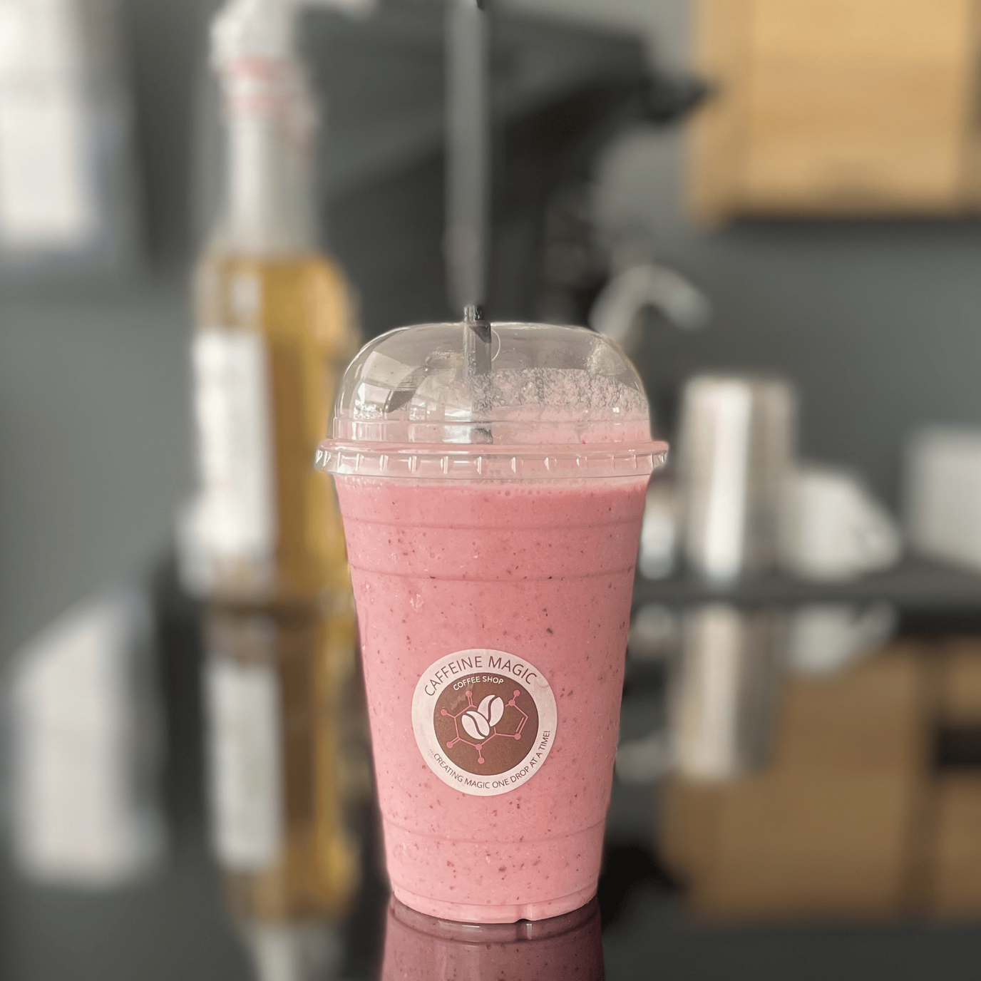 A pink smoothie with a straw in a plastic cup on a table.
