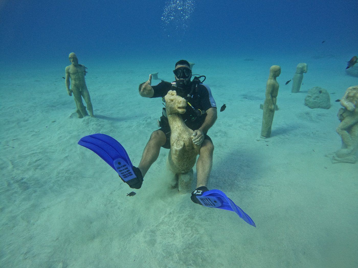 A scuba diver is riding a statue in the ocean