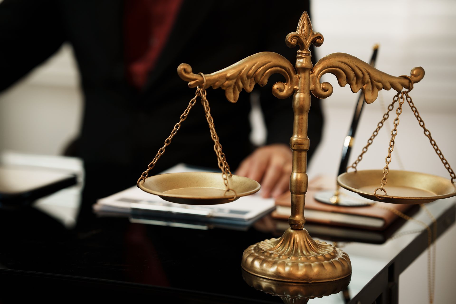 Bronze scales of justice on a desk with an attorney in the background.