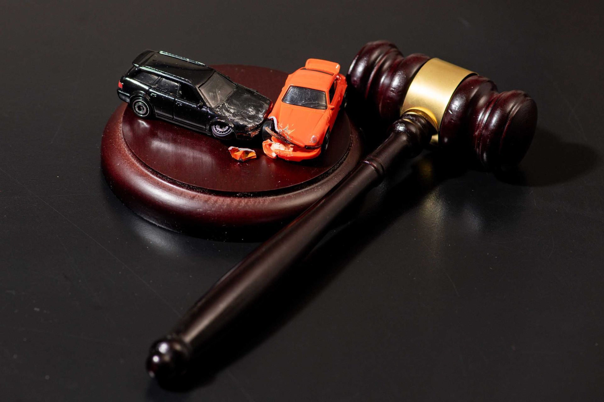 two toy cars with visible front-end damage placed on a wooden judge's gavel.