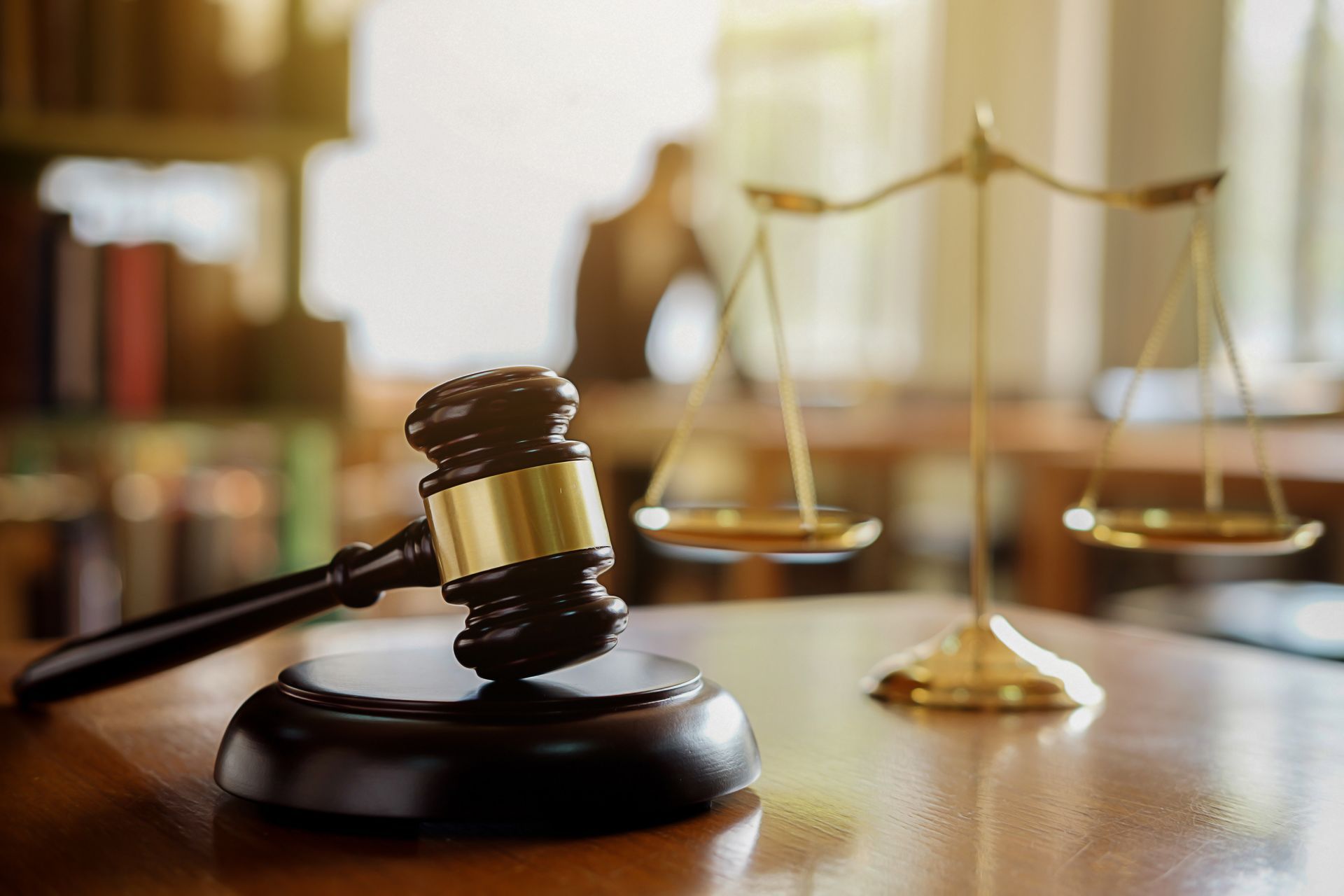 Gavel and scales of justice on a table in a library setting, symbolizing law and judgment.