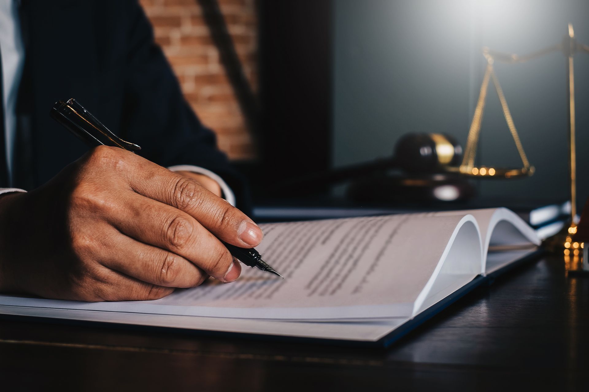 Person in a suit signing legal documents with a pen; scales of justice and a gavel in the background.