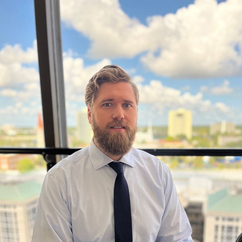 Man with beard and tie in office, city skyline background.