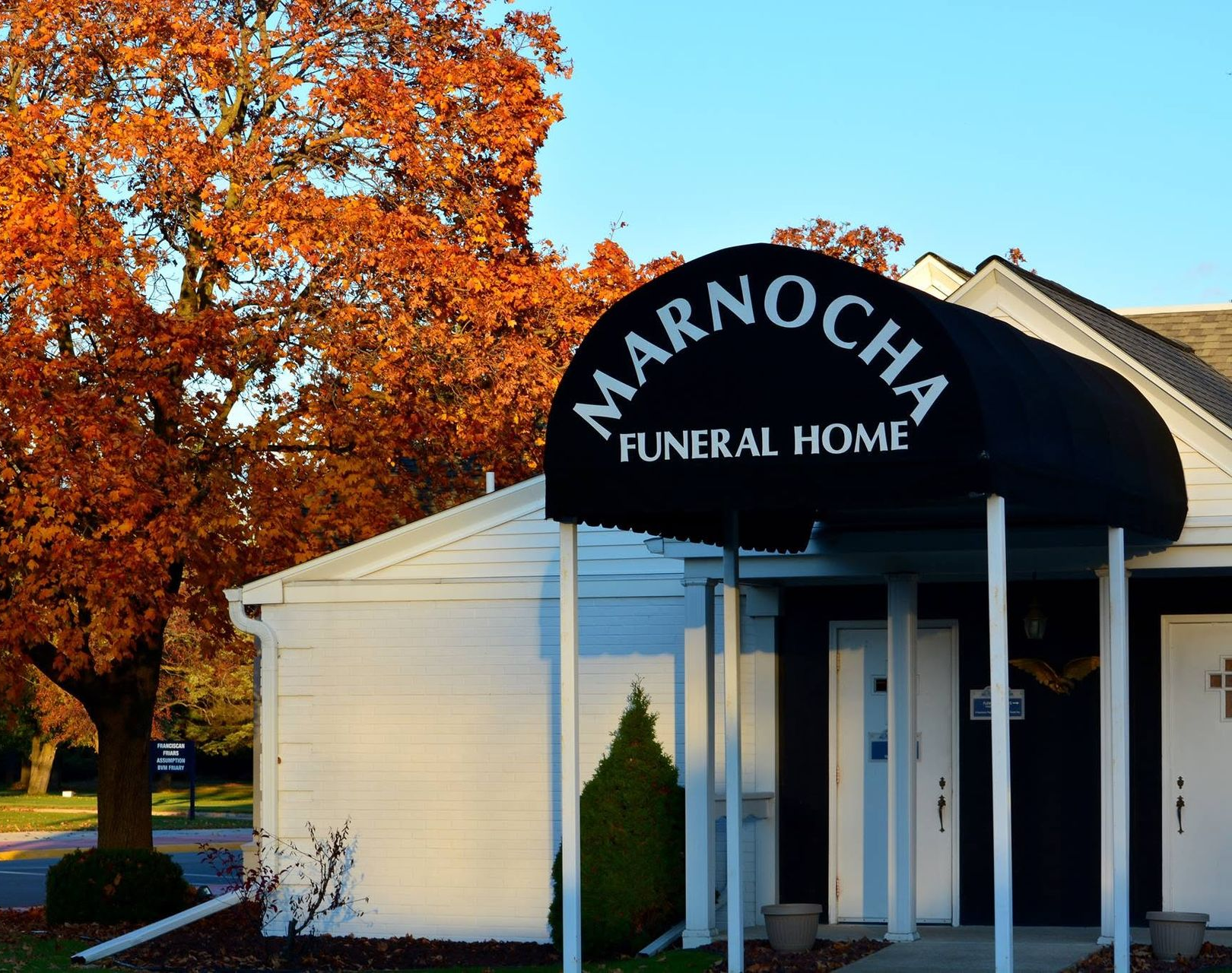 Marnocchi Funeral Home entrance with black awning, white building, and orange autumn trees