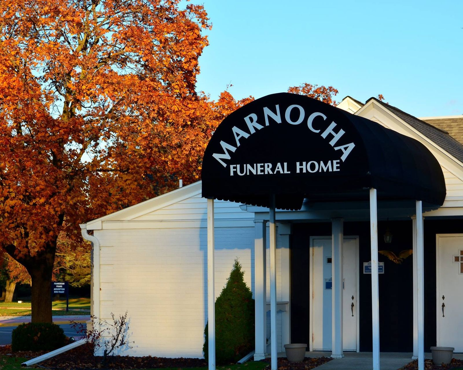 Marnocha Funeral Home entrance with black awning, white building, and autumn tree beside it