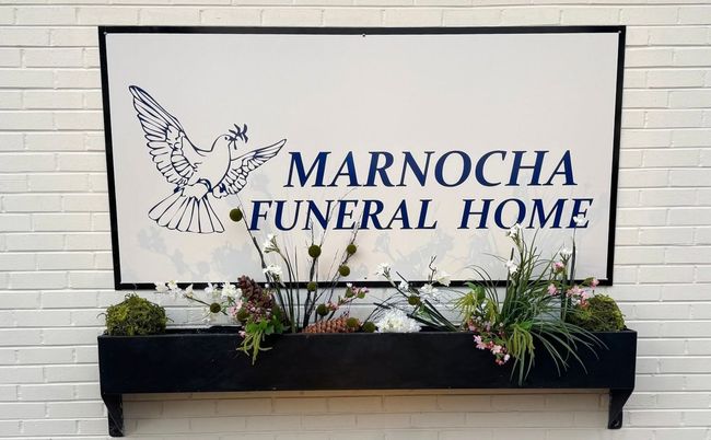 Marocha Funeral Home sign on a white brick wall above a flower box