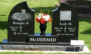 Black cemetery headstone with red flowers and engraved names Douglas D. and Leah M. McDermid