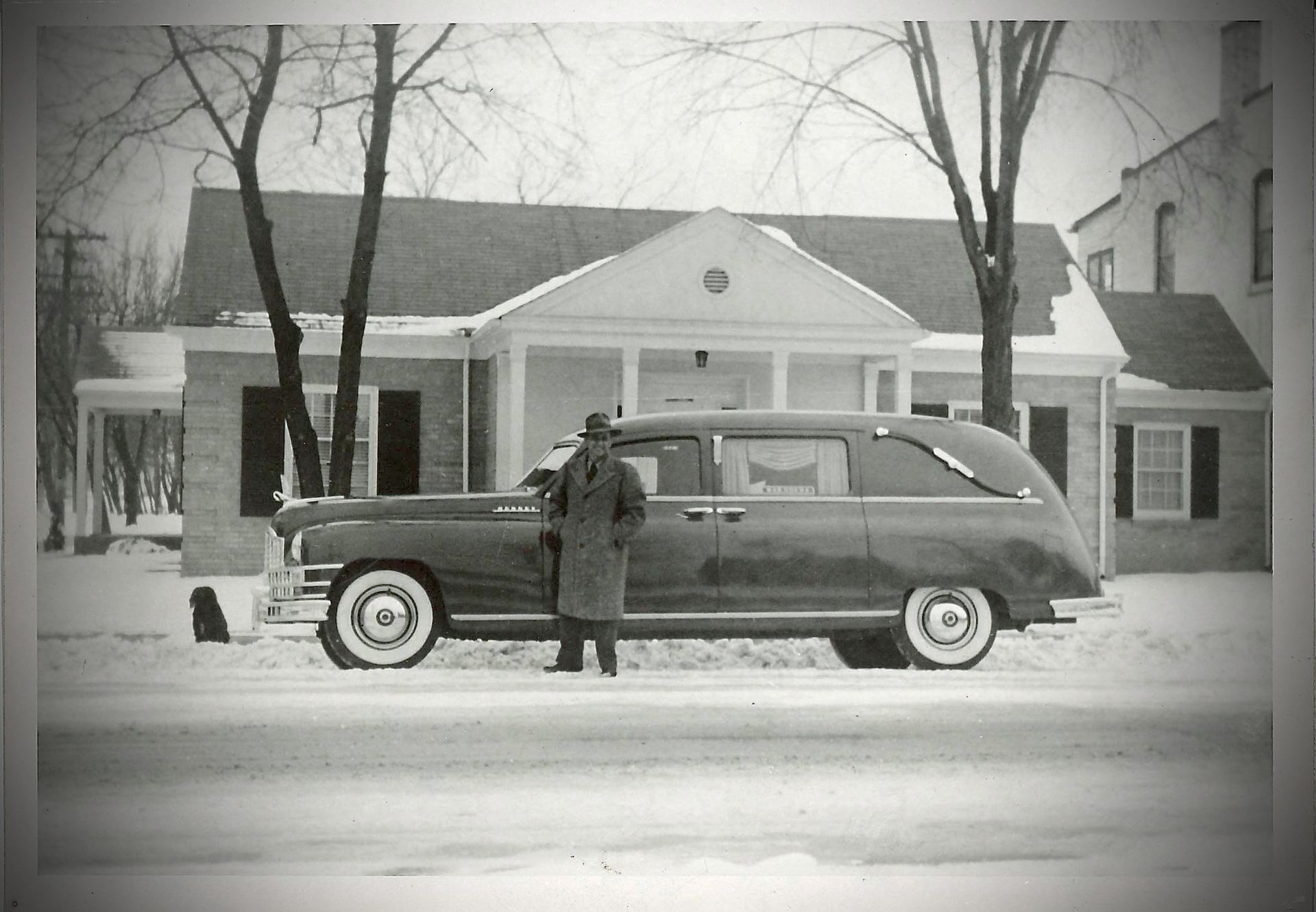 Vintage station wagon parked in front of a building, with a person standing beside it on a snowy street.