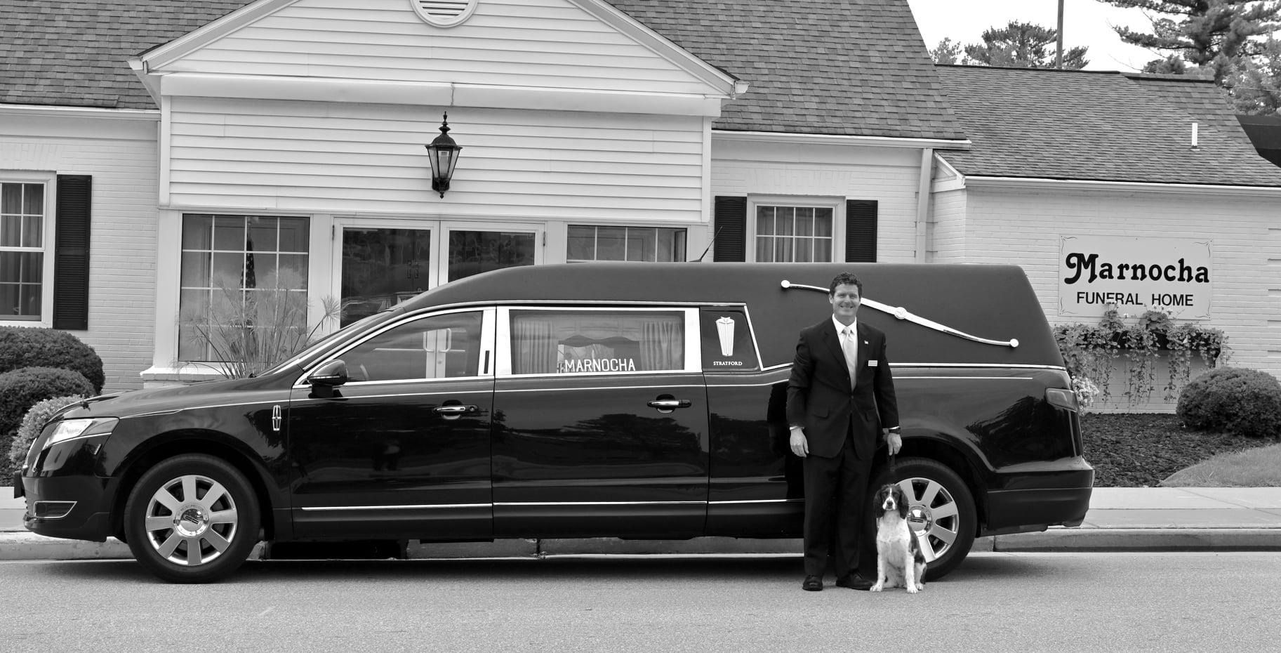 Black stretch limousine parked outside a building, with a man standing beside it and a dog near the front wheel.