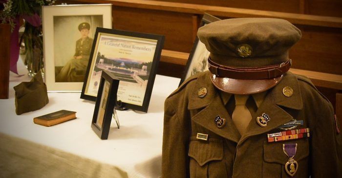 Military uniform on display beside framed photos and a commemorative plaque in a museum exhibit.