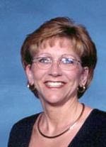 Smiling person with short brown hair and glasses against a blue background